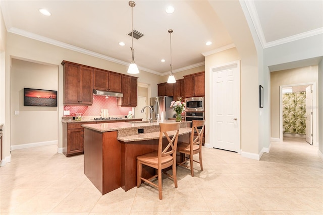 kitchen featuring stainless steel appliances, light stone counters, pendant lighting, sink, and a kitchen island with sink