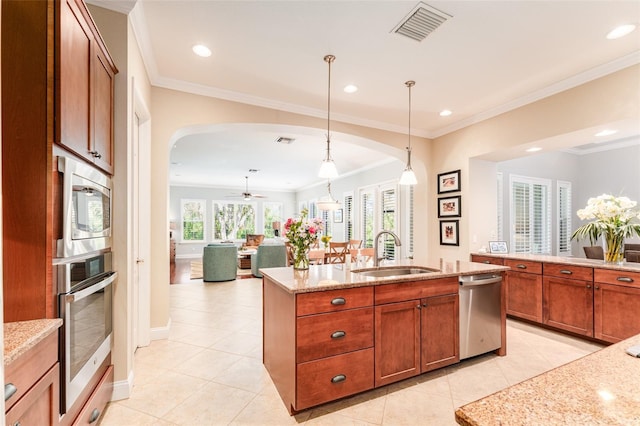 kitchen featuring a kitchen island with sink, hanging light fixtures, sink, light stone counters, and appliances with stainless steel finishes