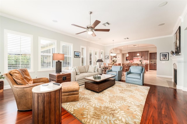 living room with dark wood-type flooring, crown molding, and ceiling fan