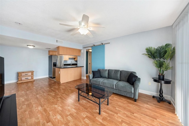 living area with a barn door, baseboards, visible vents, a ceiling fan, and light wood-style flooring