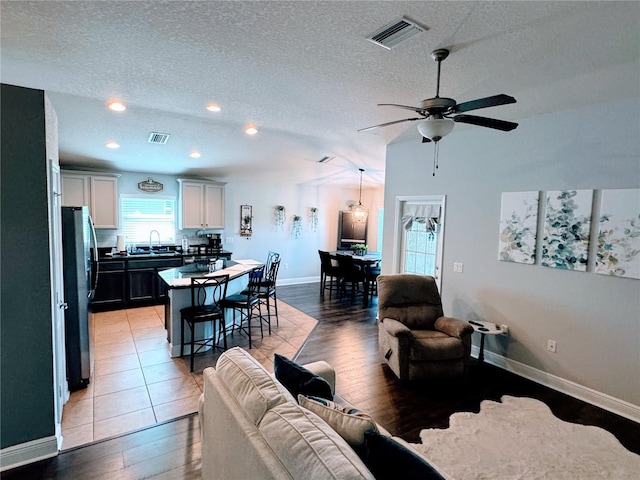 living room with sink, vaulted ceiling, a textured ceiling, and hardwood / wood-style floors