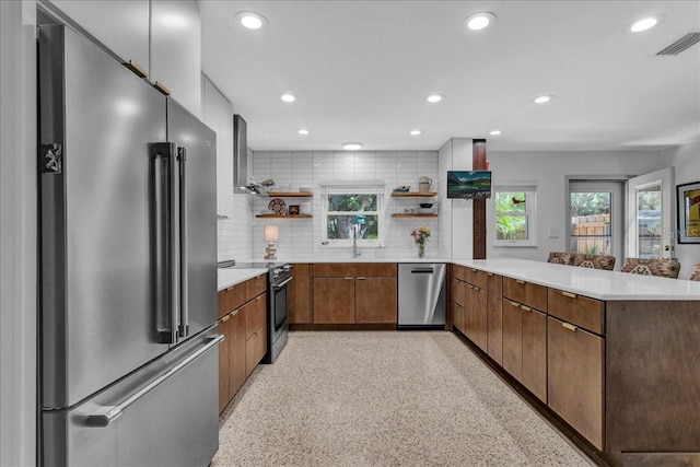 kitchen featuring appliances with stainless steel finishes, a healthy amount of sunlight, wall chimney exhaust hood, and kitchen peninsula