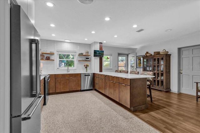 kitchen with appliances with stainless steel finishes, hardwood / wood-style floors, a breakfast bar area, decorative backsplash, and kitchen peninsula