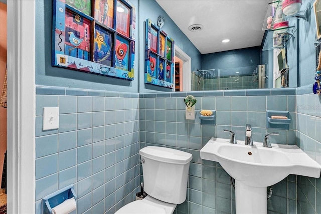 bathroom with a shower, sink, tile walls, and toilet