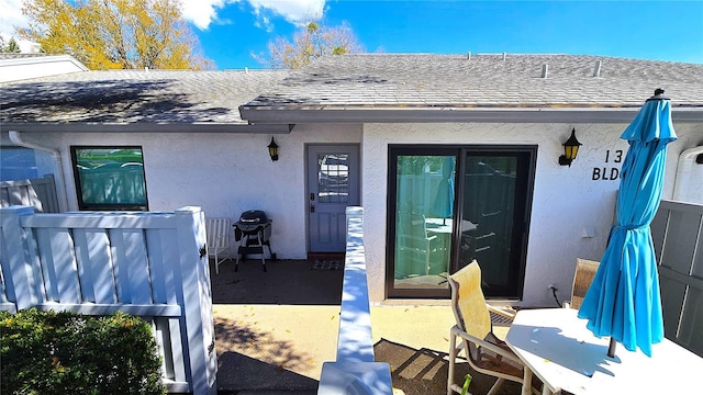 view of exterior entry featuring roof with shingles and stucco siding