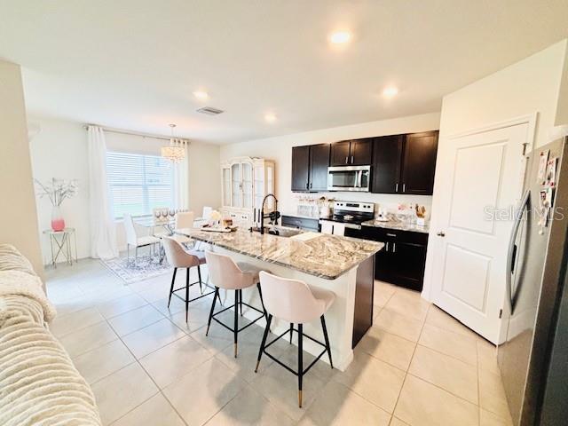 kitchen featuring sink, a breakfast bar area, hanging light fixtures, stainless steel appliances, and a center island with sink