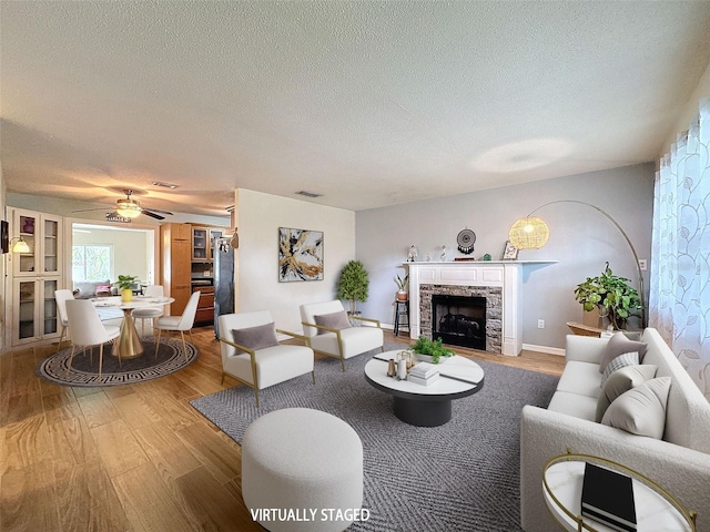 living room featuring a textured ceiling, a fireplace, visible vents, and wood finished floors