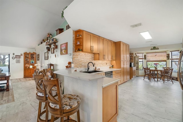 kitchen with a kitchen bar, sink, kitchen peninsula, dishwasher, and backsplash