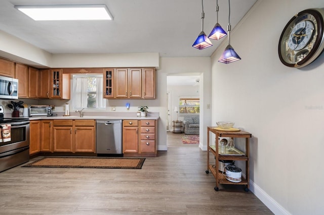 kitchen with light wood-type flooring, decorative light fixtures, plenty of natural light, and appliances with stainless steel finishes