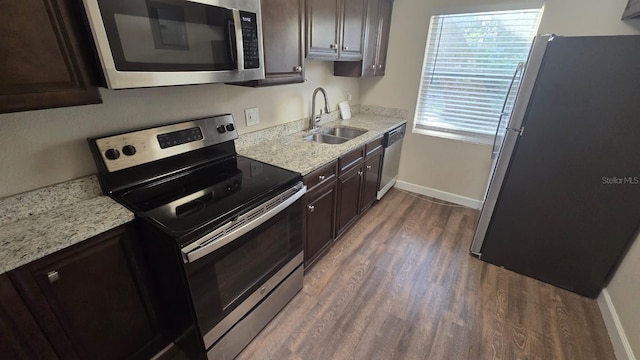 kitchen featuring dark wood-type flooring, dark brown cabinetry, sink, stainless steel appliances, and light stone countertops