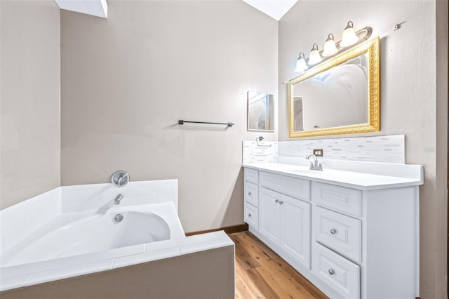 bathroom with tasteful backsplash, vanity, hardwood / wood-style floors, and tiled bath