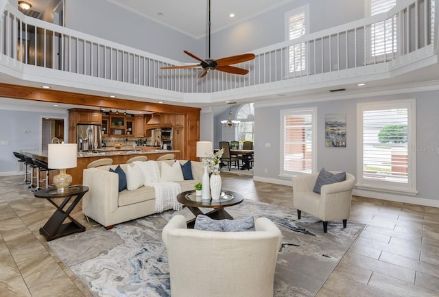 living room with a towering ceiling, ornamental molding, and ceiling fan with notable chandelier