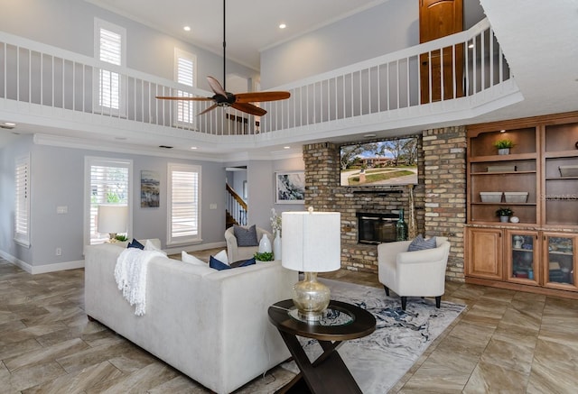 living room featuring crown molding, a brick fireplace, a towering ceiling, and ceiling fan