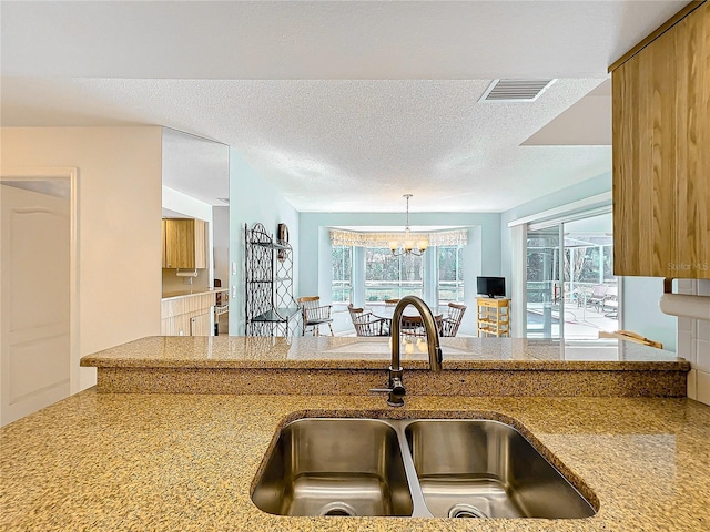 kitchen featuring pendant lighting, sink, a textured ceiling, and a chandelier