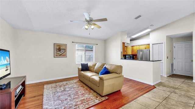 living room featuring a textured ceiling, vaulted ceiling, ceiling fan, and light wood-type flooring