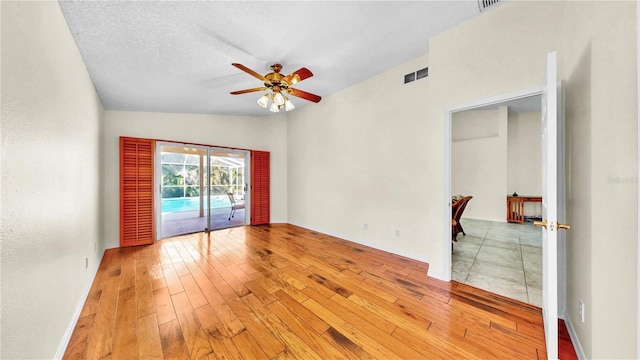 empty room featuring ceiling fan, lofted ceiling, a textured ceiling, and light wood-type flooring