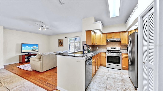 kitchen with sink, dark stone countertops, appliances with stainless steel finishes, kitchen peninsula, and decorative backsplash