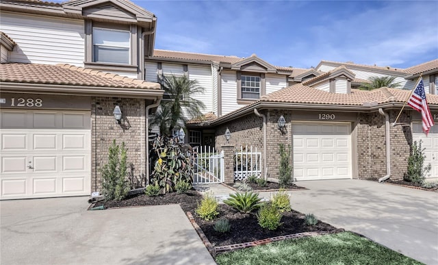 view of property with an attached garage, a tiled roof, brick siding, and concrete driveway