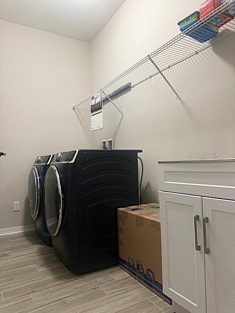 laundry area with a textured ceiling, cabinets, light hardwood / wood-style floors, and washer and clothes dryer