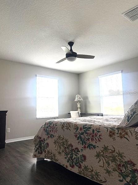 bedroom featuring ceiling fan, dark wood-type flooring, multiple windows, and a textured ceiling