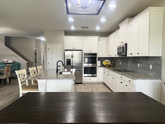 kitchen featuring white cabinetry, stainless steel appliances, a kitchen island with sink, and dark stone countertops