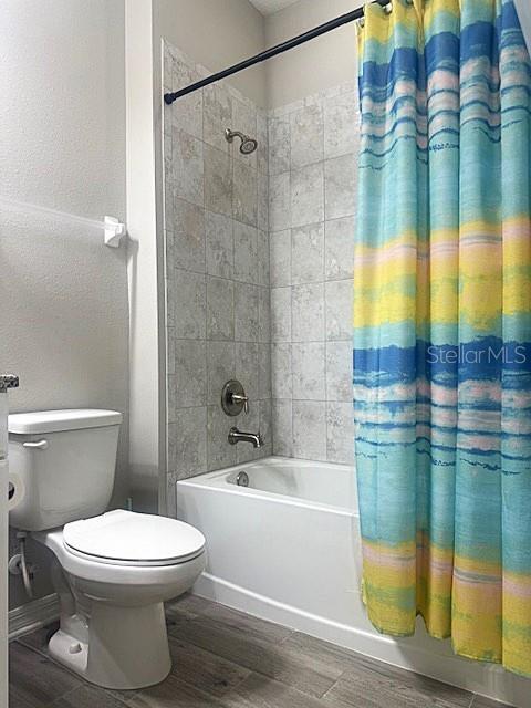 bathroom with toilet, shower / bath combination with curtain, and wood-type flooring