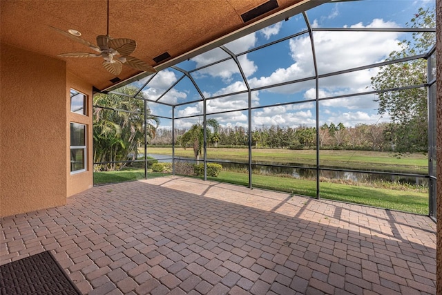 view of patio featuring ceiling fan, a water view, and glass enclosure