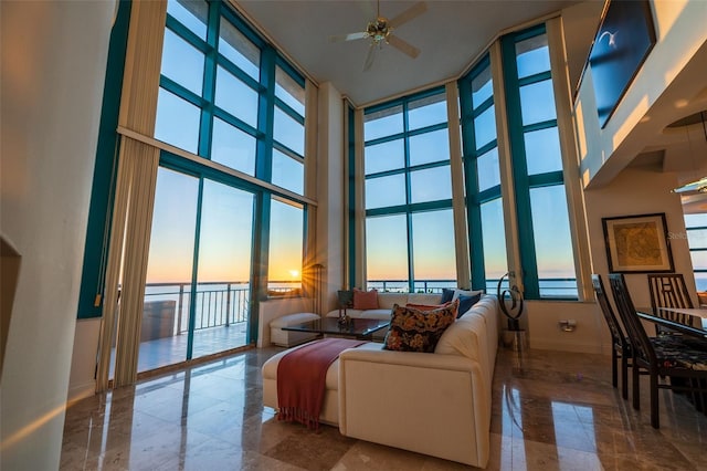 living room with ceiling fan, a wall of windows, and a towering ceiling