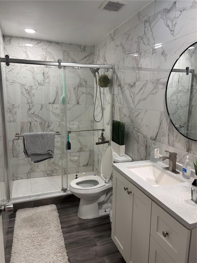 bathroom with wood-type flooring, tile walls, vanity, walk in shower, and toilet