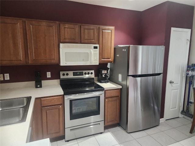 kitchen with appliances with stainless steel finishes, brown cabinetry, light countertops, and a sink