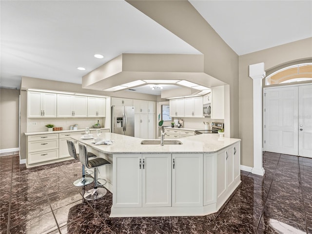 kitchen with light stone counters, stainless steel appliances, sink, and white cabinets