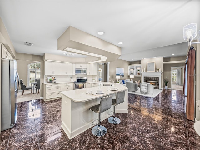 kitchen featuring white cabinetry, appliances with stainless steel finishes, a kitchen bar, and plenty of natural light