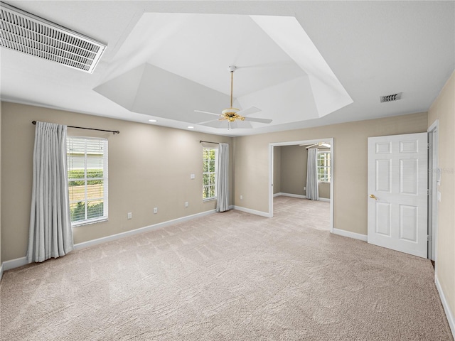 unfurnished room featuring ceiling fan, a tray ceiling, light carpet, and a wealth of natural light