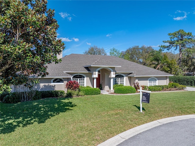 ranch-style house featuring roof with shingles, a front lawn, and stucco siding