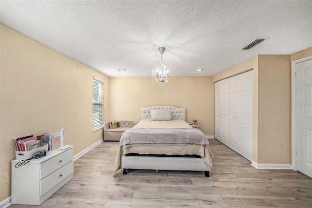 bedroom with an inviting chandelier, a closet, a textured ceiling, and light wood-type flooring