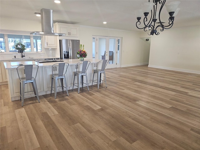 kitchen featuring island range hood, a breakfast bar, white cabinets, light countertops, and stainless steel fridge