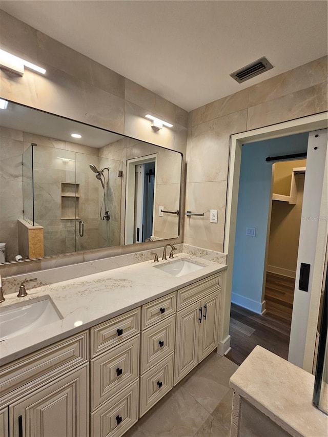 full bath featuring double vanity, a stall shower, visible vents, and a sink