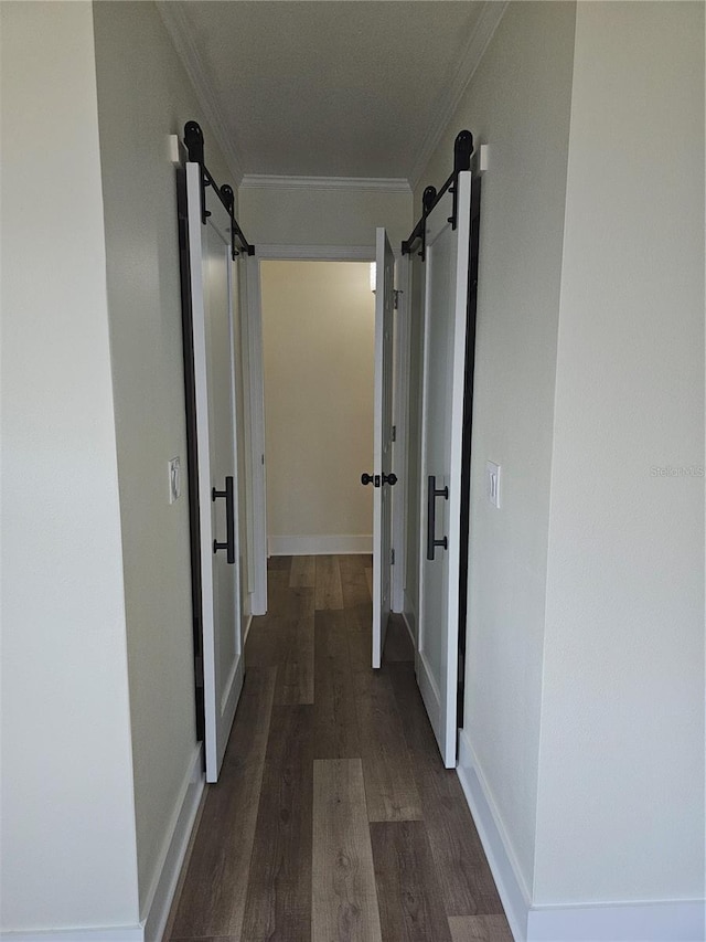 corridor featuring a barn door, baseboards, dark wood-style flooring, and crown molding