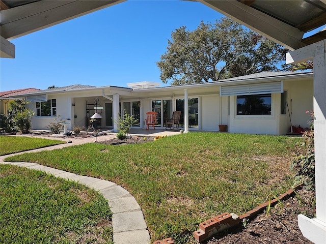 back of house with stucco siding and a yard