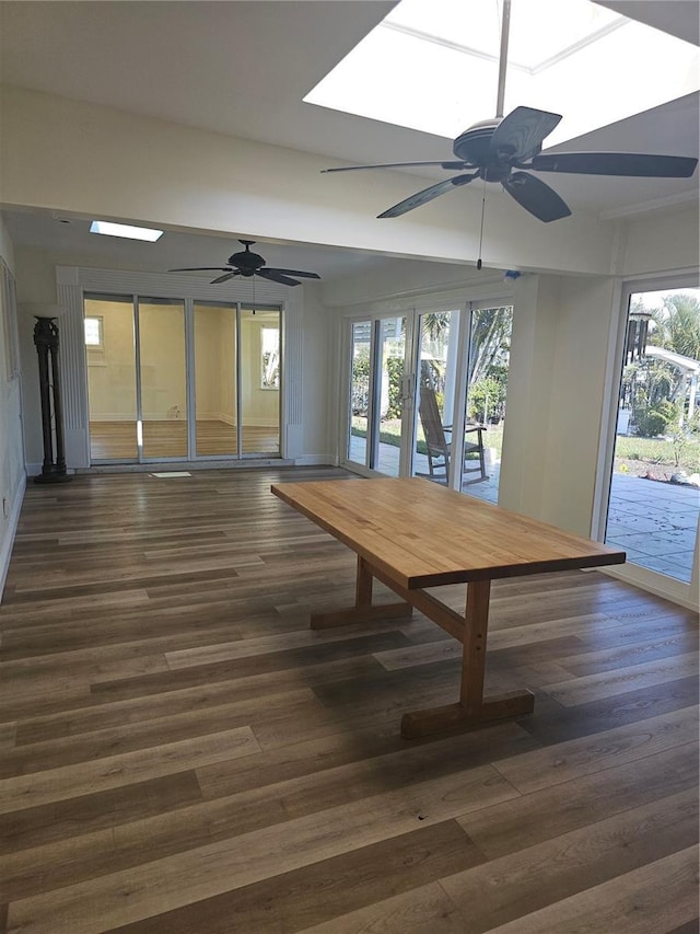 unfurnished dining area featuring a skylight, dark wood finished floors, and a ceiling fan