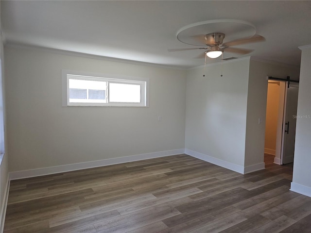 empty room featuring dark wood-style floors, a barn door, ornamental molding, and baseboards