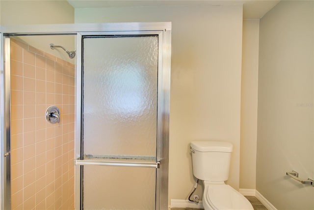 bathroom with baseboards, a shower stall, and toilet