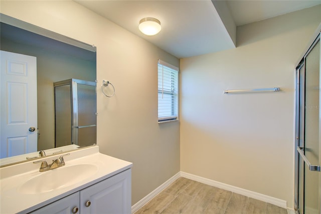 bathroom with a stall shower, wood finished floors, vanity, and baseboards