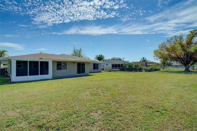 back of house featuring a sunroom, a fenced backyard, stucco siding, and a yard