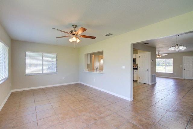 empty room featuring ceiling fan with notable chandelier, light tile patterned floors, visible vents, and baseboards