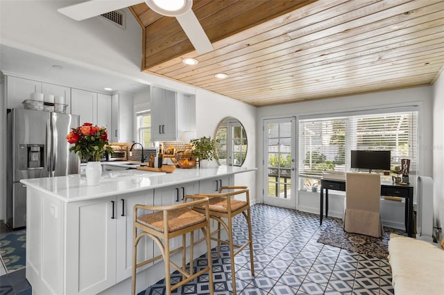 kitchen featuring tasteful backsplash, white cabinets, a kitchen bar, stainless steel fridge, and wood ceiling