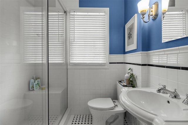 bathroom with toilet, a shower with shower door, sink, and tile walls