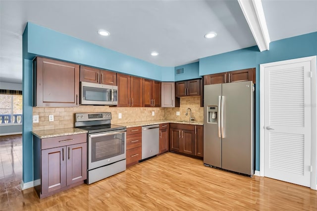 kitchen featuring sink, stainless steel appliances, tasteful backsplash, light stone counters, and light wood-type flooring