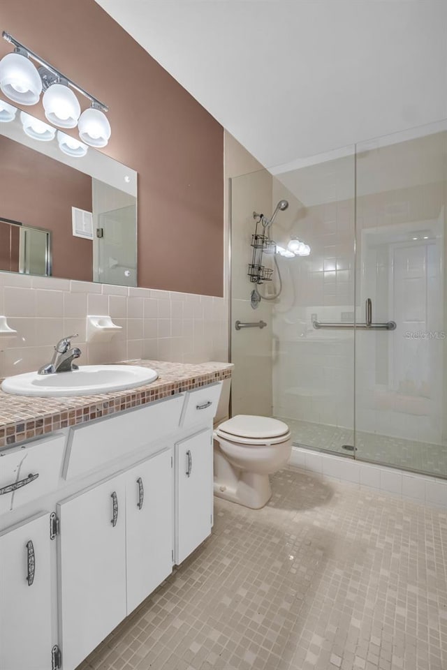 bathroom featuring a shower with door, tile walls, vanity, tile patterned floors, and toilet