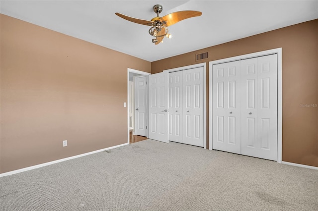 unfurnished bedroom with two closets, ceiling fan, and carpet